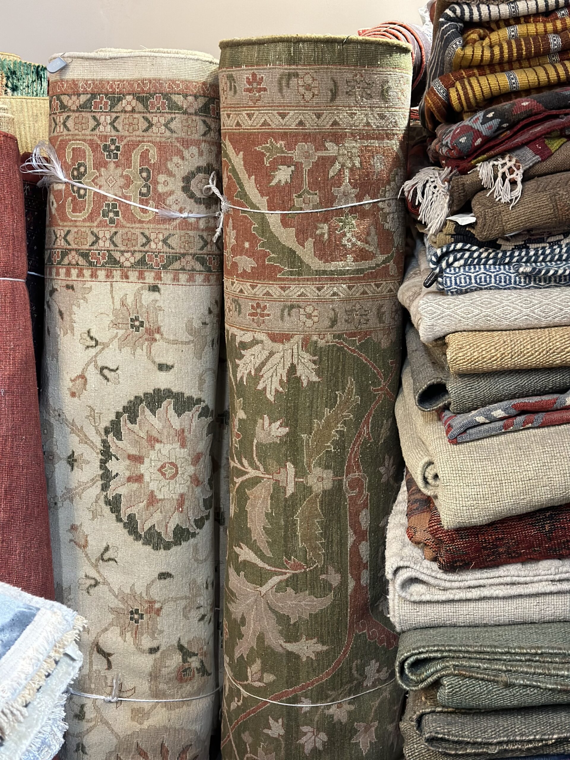 Two hand knotted rugs rolled up along with a stack of other rugs